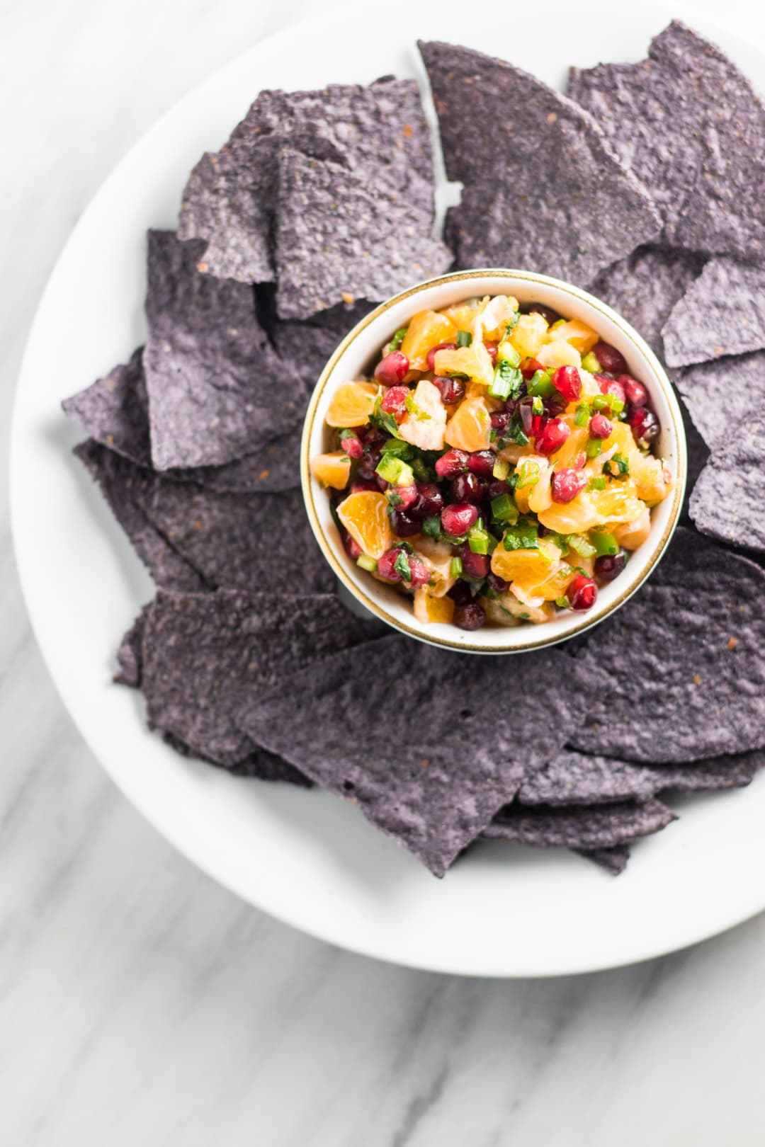 Low FODMAP Pomegranate Orange Salsa in a small white bowl surrounded by blue corn tortilla chips.