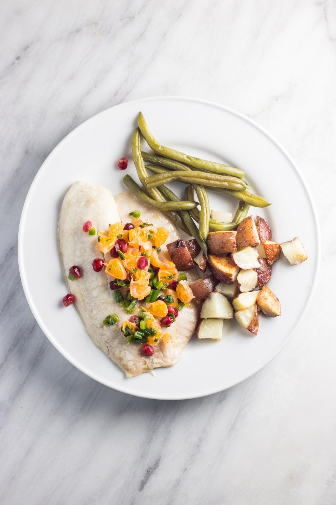Low FODMAP Pomegranate Orange Salsa on baked white fish with green beans and roasted potatoes on a white plate. 