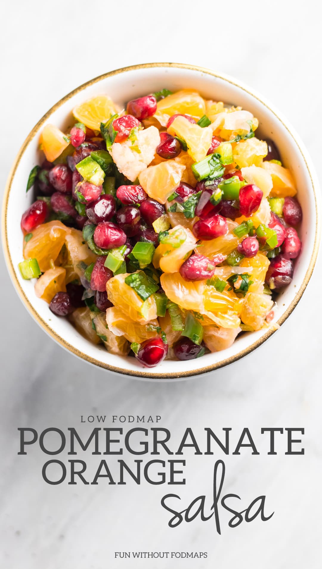 Low FODMAP Pomegranate Orange Salsa in a white bowl sitting on a white marble background with a gray text overlay of the recipe name. 