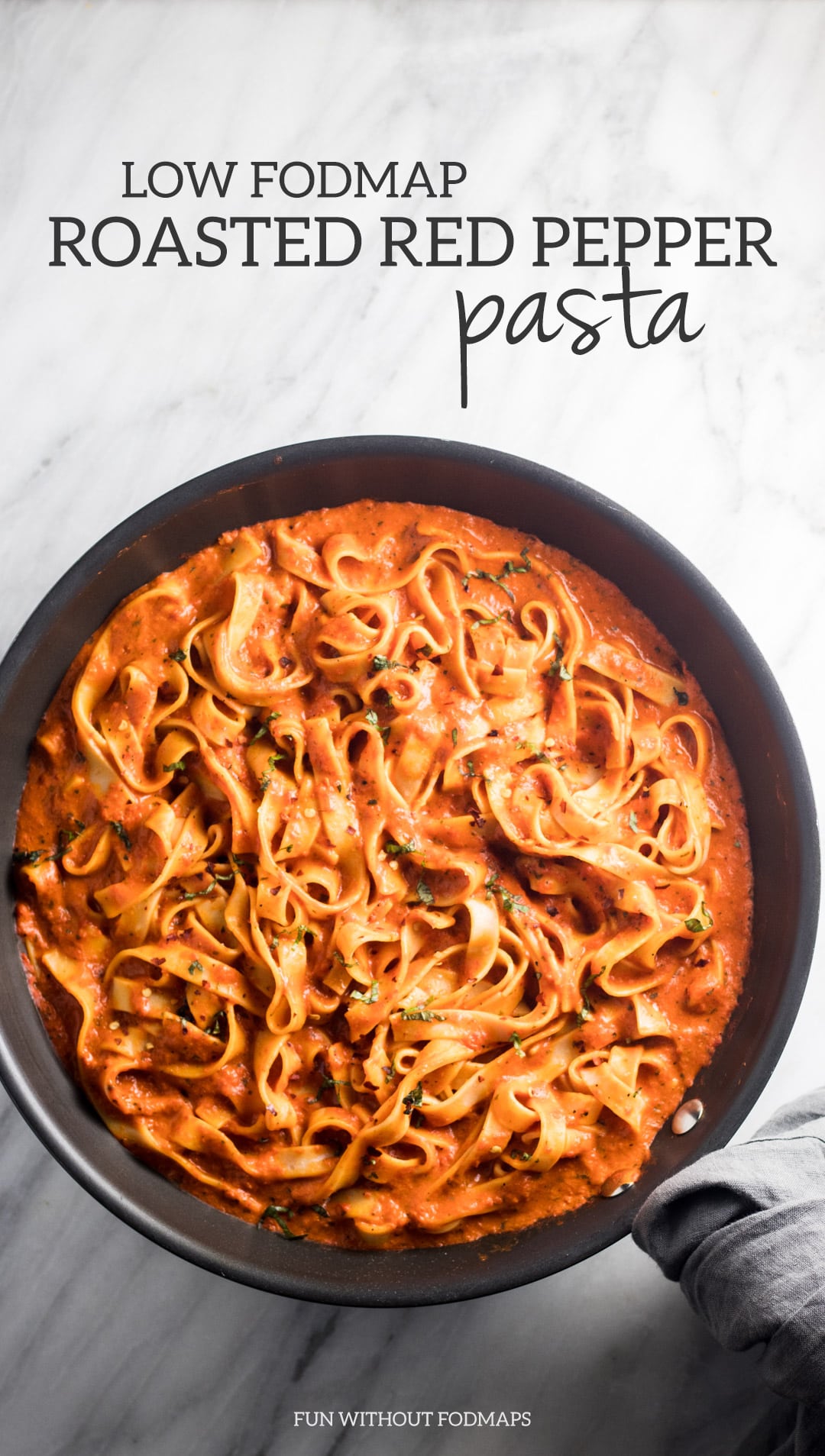 Looking down at a skillet filled with fettuccini tossed in a red pepper sauce. The skillet handle is wrapped in a gray linen napkin. Above the skillet a black text overlay reads Low FODMAP Roasted Red Pepper Pasta