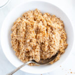 An overhead shot of a large white bowl filled with Instant Pot Low FODMAP Steel Cut Oats. There is an antique serving spoon grabbing a scoop.