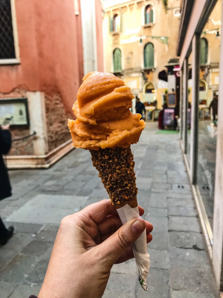 Persimmon sorbetto with a gluten-free cone dipped in chocolate and dusted with chopped hazelnuts from Grom in Venice Italy