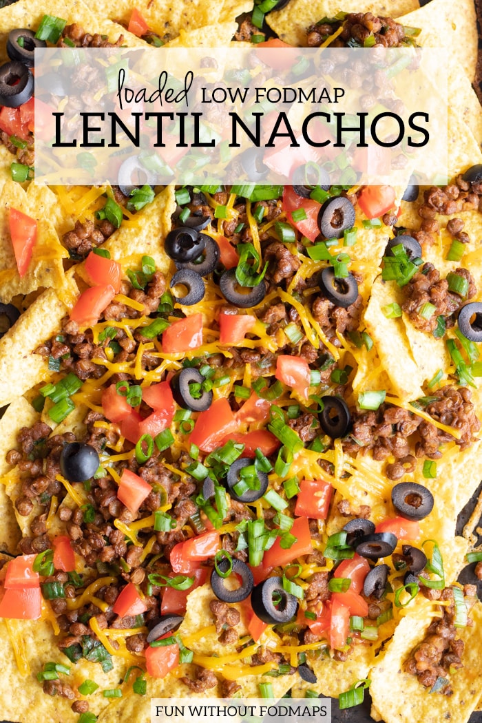 Close up of loaded low FODMAP lentil nachos topped with diced fresh tomatoes, black olives, and the sliced green tops of green onions. A white faded rectangle is centered at the top and filled with dark gray text that reads loaded low FODMAP lentil nachos.