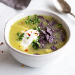 A small white bowl filled with low FODMAP chicken enchilada soup. An antique spoon and dark gray napkin peek into the background.