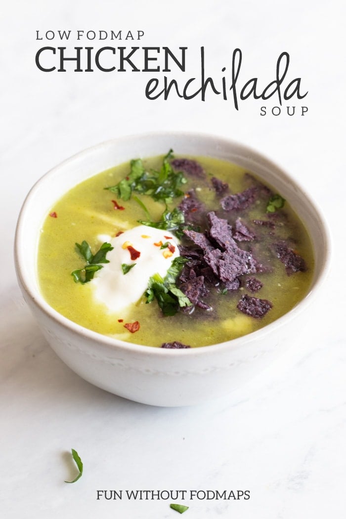 A small white bowl filled green enchilada chicken soup. The soup is topped with fresh cilantro, crushed blue corn chips, fresh cilantro, and red pepper flakes. The bowl is set on a white marble background. On the top of the image gray text reads Low FODMAP Chicken Enchilada Soup. At the bottom of the image gray text reads FUN WITHOUT FODMAPS. 
