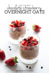 Two clear glasses filled with overnight oats and topped with diced strawberries and mini chocolate chips. There are strawberries and mini chocolate chips scattered around them on the white marble slab everything is sitting on. Centered dark gray text reads low FODMAP chocolate strawberry overnight oats at the top of the image.