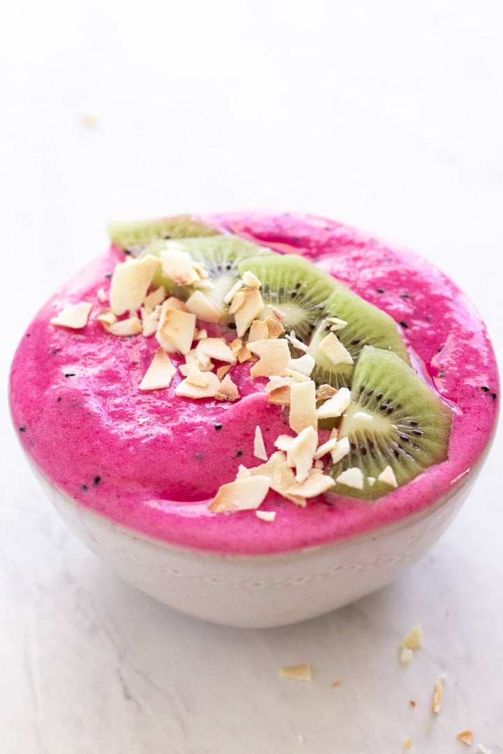 A low FODMAP dragon fruit smoothie bowl sits on a white marble slab.