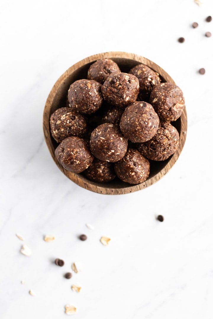 An overhead shot of a bowl filled with low FODMAP peanut butter chocolate bites on a white marble background. A few chocolate chips and rolled oats are scattered about. 