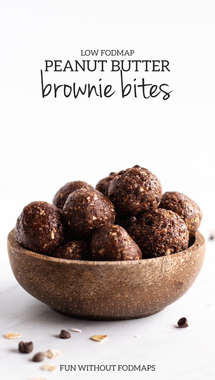 A dark wooden bowl sits on white marble slab. The bowl is filled with energy bites and there are chocolate chips and oats scattered sporadically in the foreground. The upper part of the image is faded to white with black text reading low FODMAP peanut butter brownie bites. The words FUN WITHOUT FODMAPS in black text is centered at the bottom.