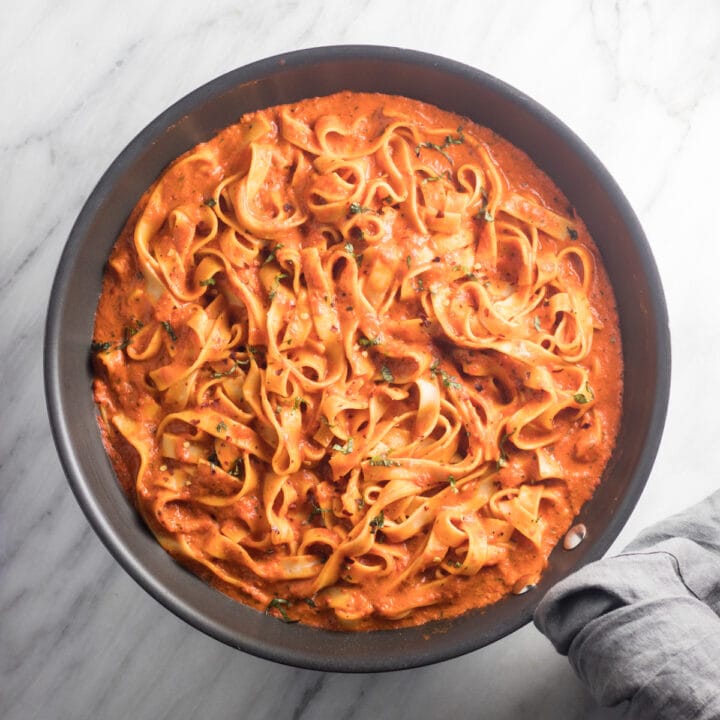 Looking down at a skillet filled with fettuccine tossed with a roasted red pepper sauce.