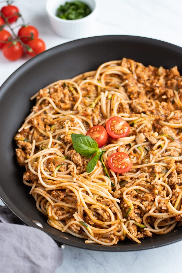 A black skillet is filled with low FODMAP spaghetti and zoodles. Three cherry tomato halves and a couple of basil leaves are artistically placed in the center of the skillet. 