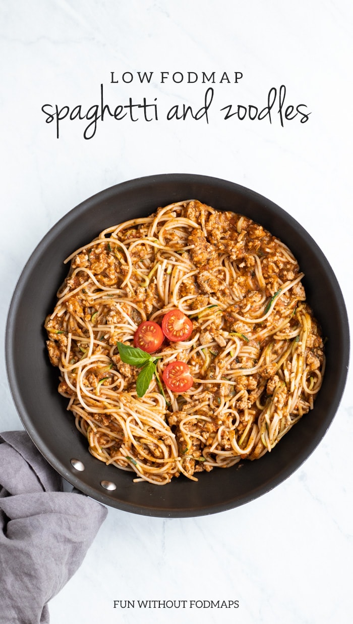 An overhead shot of a skillet sitting on a white marble slab. The skillet is filled with cooked spaghetti and topped with a couple of cherry tomato halves. The skillet's handle is wrapped in a dark gray napkin. At the top of the image, dark gray text reads low FODMAP spaghetti and zoodles and FUN WITHOUT FODMAPS is centered at the bottom.