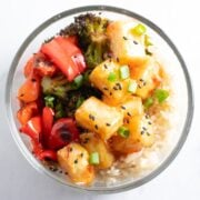 A glass pyrex bowl filled with Low FODMAP Sweet Chili Tofu Bowls or crispy tofu tossed in a sweet chili sauce, roasted broccoli, red pepper, and carrots, and whole grain rice.