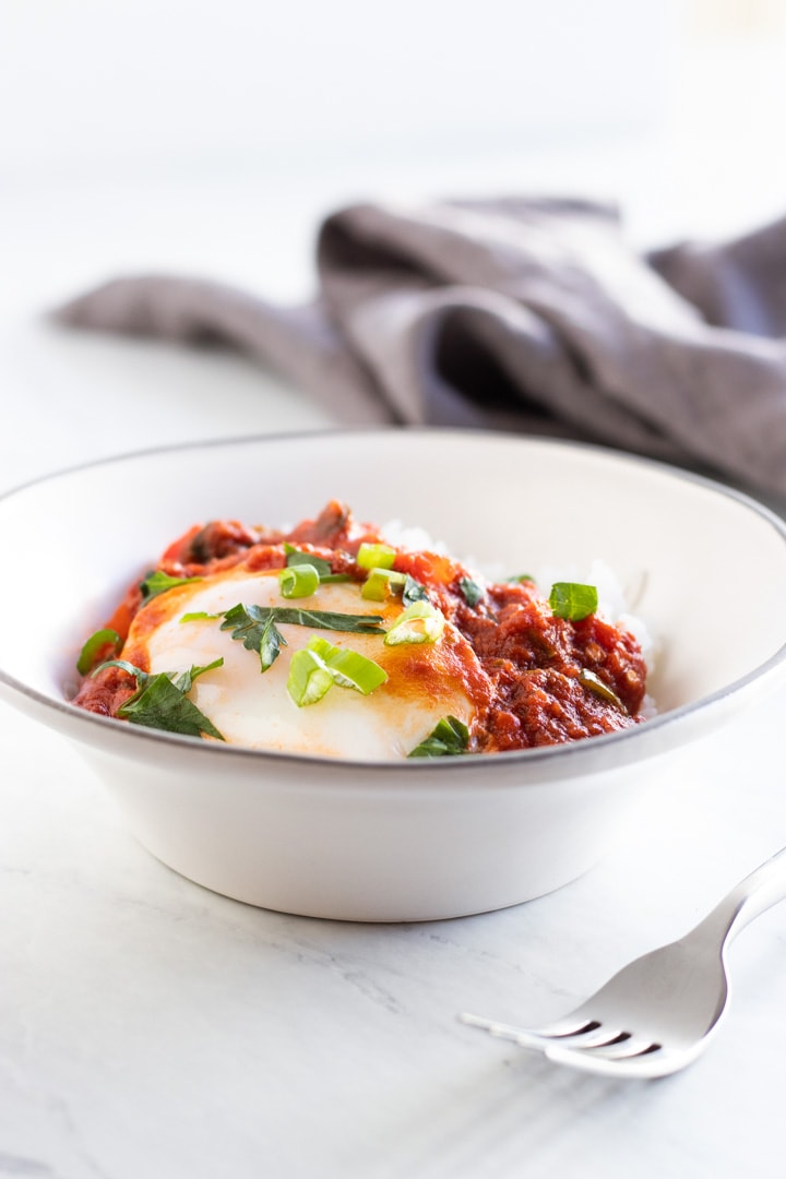 A bowl filled with rice topped with low FODMAP shakshuka. A fork is in the foreground and a dark gray napkin in the background.