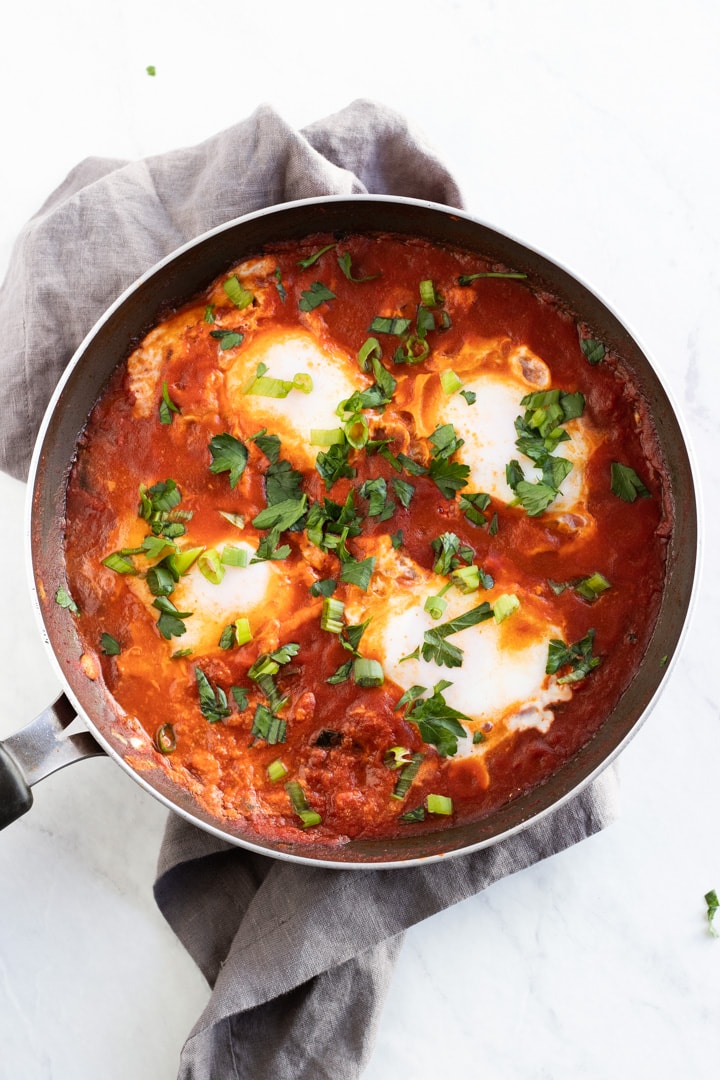 An overhead shot of a skillet filled with low FODMAP shakshuka on a white marble slab.