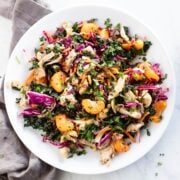 A colorful plate of kale, red cabbage, clementines, carrots, chicken and herbs.