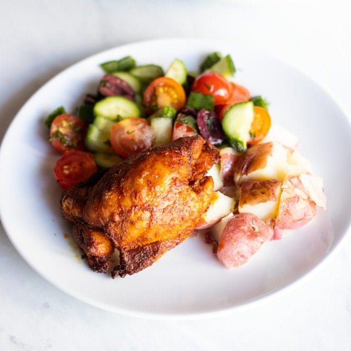 A plate with Moroccan chicken, baby red potatoes, and a cucumber, tomato, and dill salad.