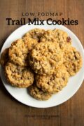 A plate of oatmeal cookies dotted with chocolate chips, dried cranberries and pecans. A black text overlay reads "Low FODMAP Trail Mix Cookies"