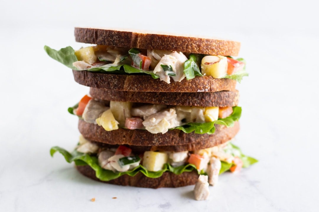 A stack of three sandwiches made with chicken, pineapple, and red bell pepper.