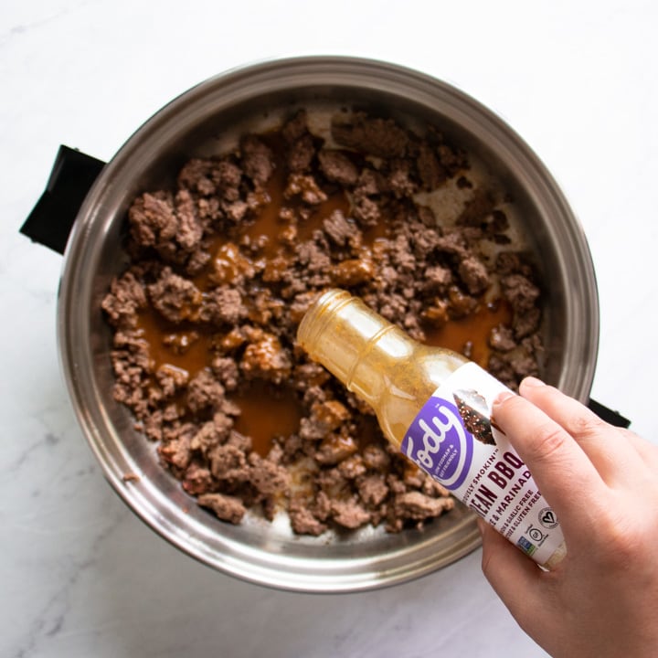 A bottle of FODY Foods Korean BBQ pouring into a skillet filled with browned beef.