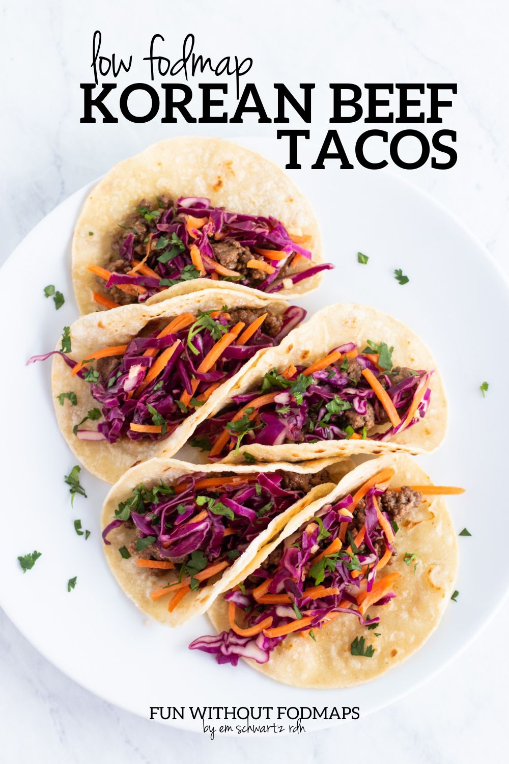 A plate of five corn tortilla tacos filled with ground beef and pickled carrots and red cabbage. In the white space above, black text reads "Low FODMAP Korean Beef Tacos".