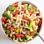 A serving spoon resting in a bowl of BLT (bacon, lettuce, tomato) pasta salad.