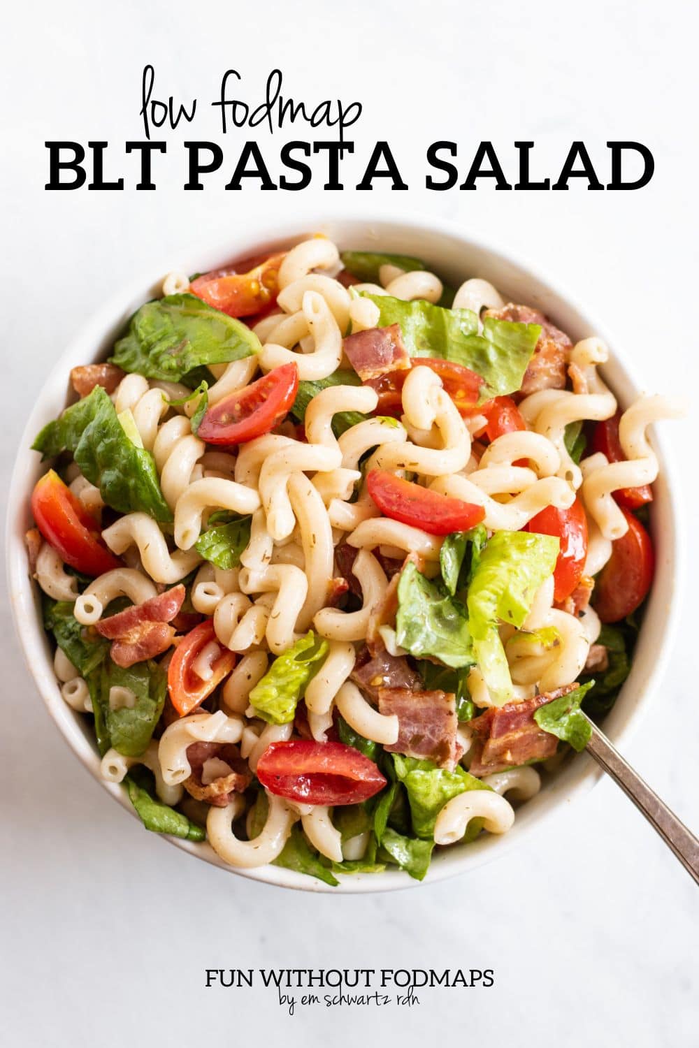 A bowl of cold pasta salad with romaine lettuce, cherry tomatoes, and bacon. In the white space above, black text reads "low FODMAP BLT Pasta Salad".