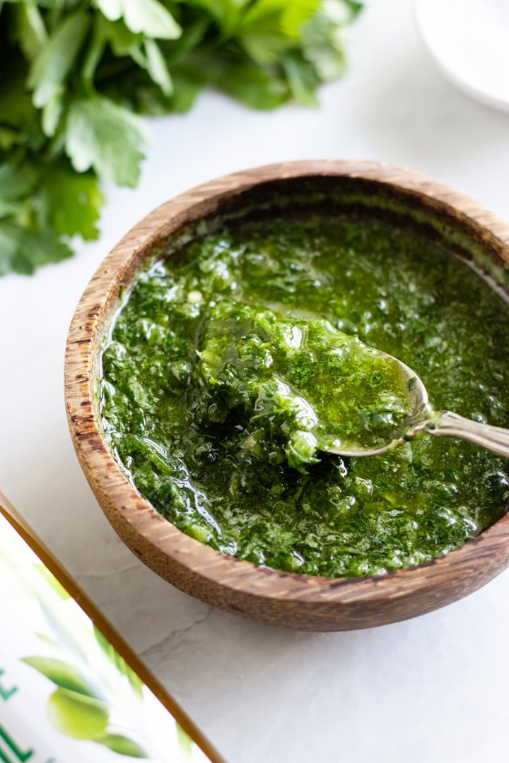 A spoon dips into a small wooden bowl filled with chimichurri, a no-cook sauce made with fresh parsley.