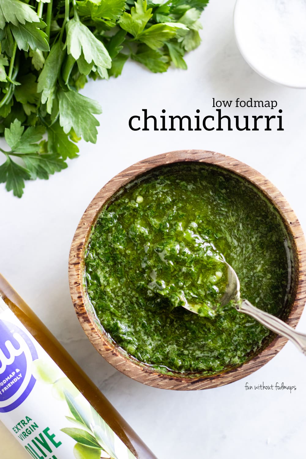 Looking down at a spoon resting in a small wooden bowl filled with chimichurri. In the white space above, black text reads "Low FODMAP Chimichurri."