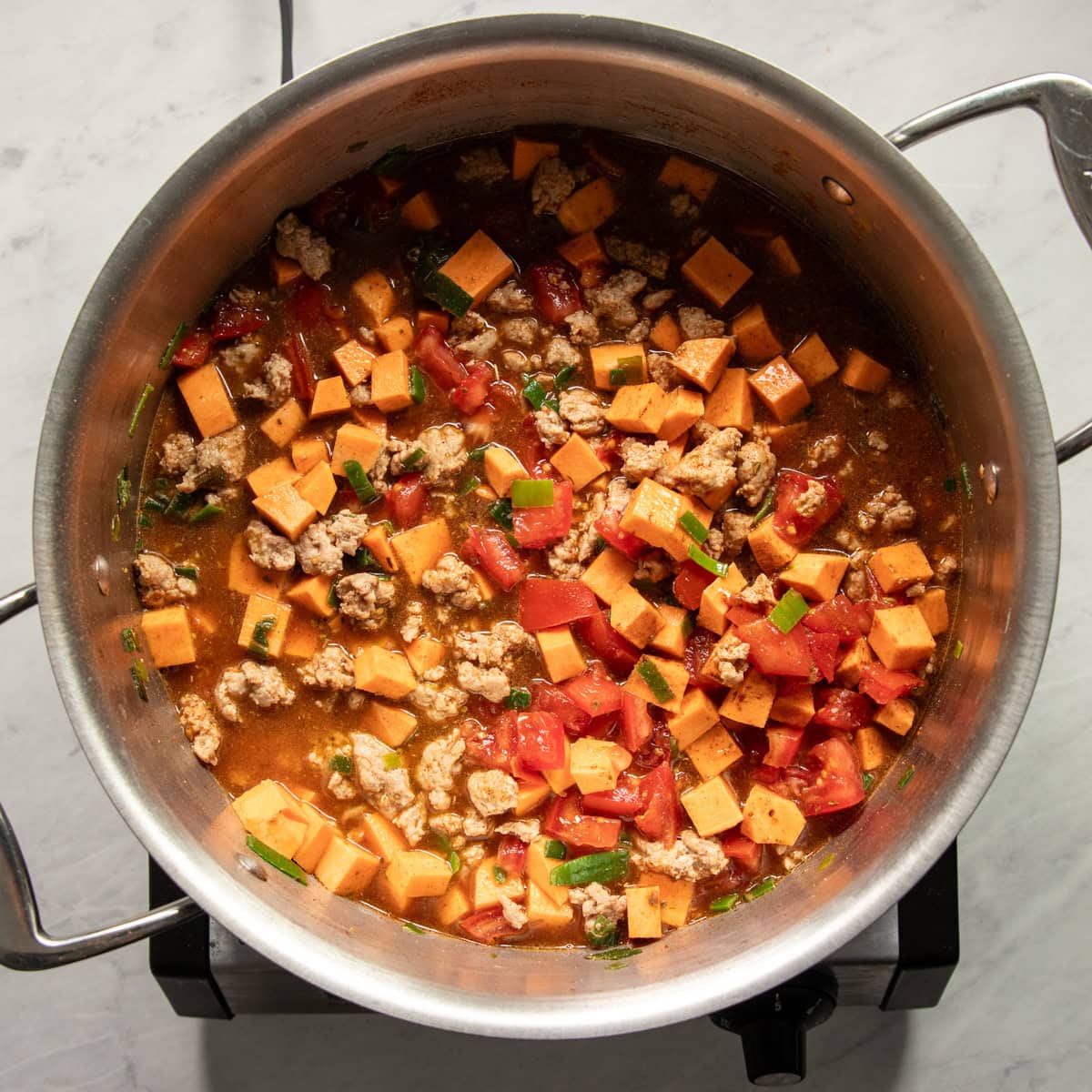 Sweet potatoes, tomatoes, spices, herbs and low FODMAP broth are added to browned turkey in a soup pot.