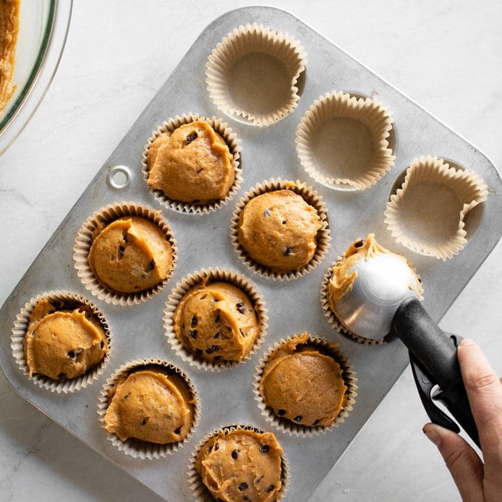 Scooping muffin batter into lined muffin tin.