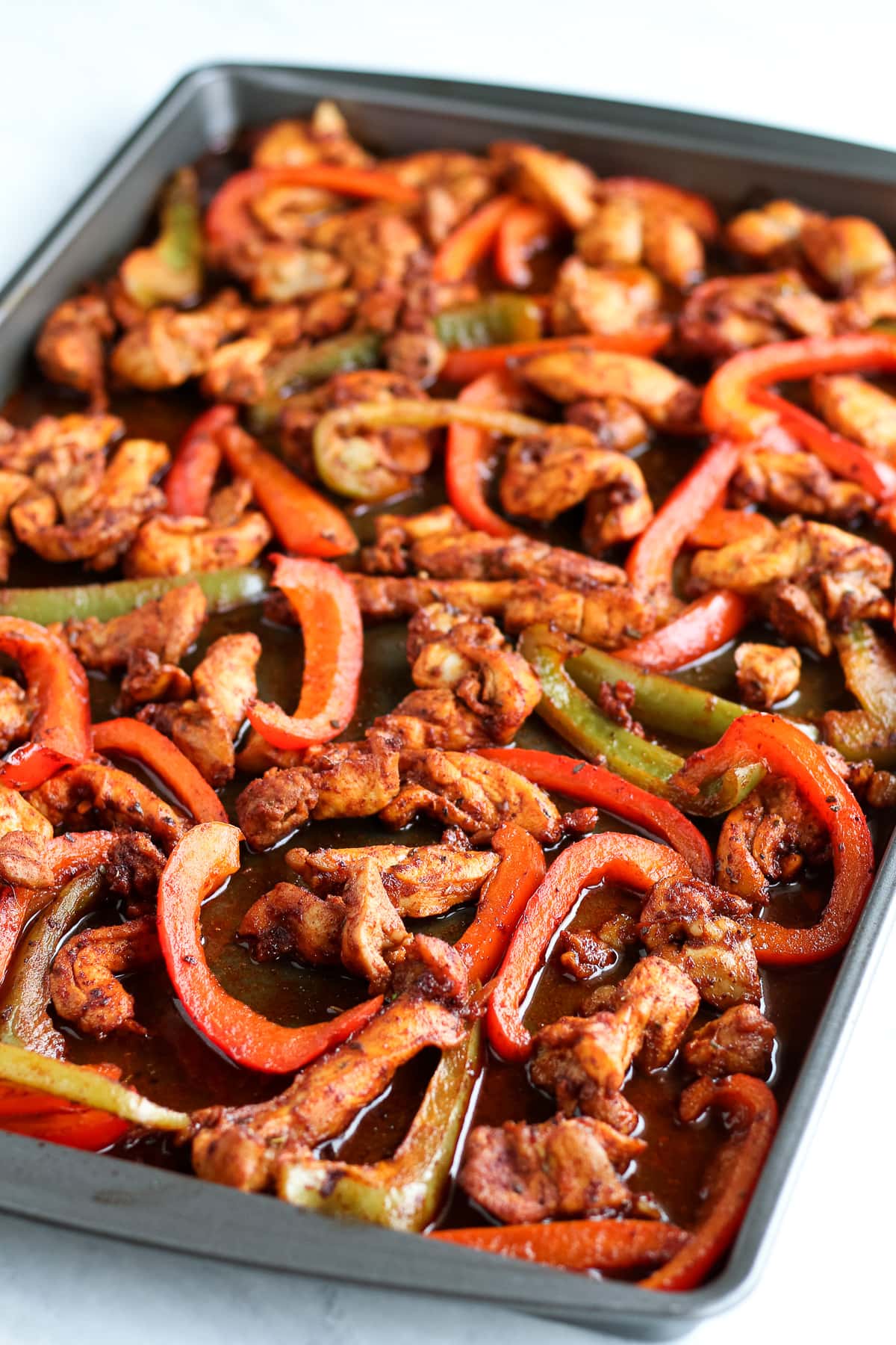A sheet pan filled with baked chicken thigh slices and sliced red and green bell peppers.