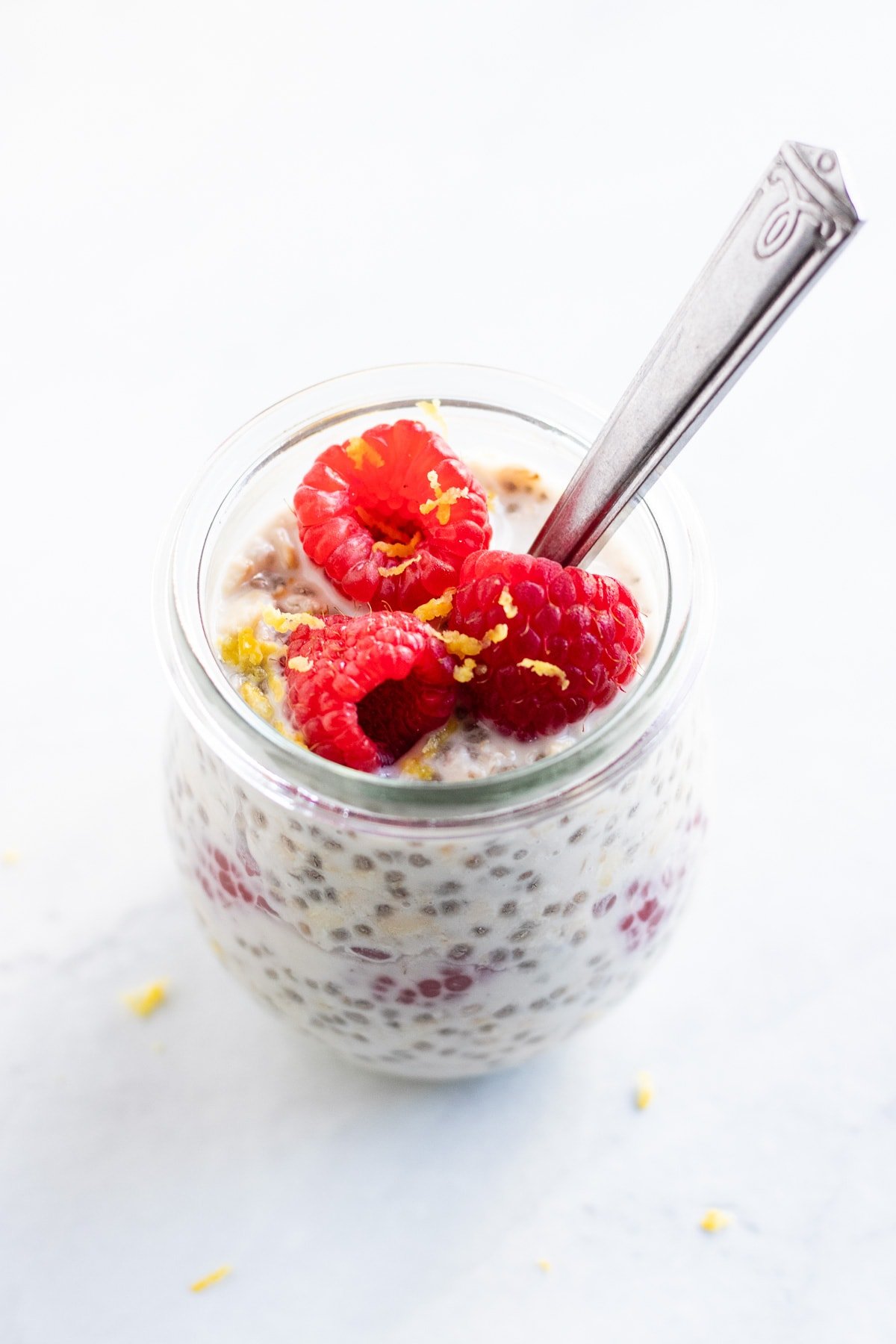 A glass tulip jar is filled with low FODMAP lemon raspberry overnight oats. Juicy raspberries flecked with fresh lemon zest sit on top. There's a spoon ready for you to dig into this easy low FODMAP breakfast!
