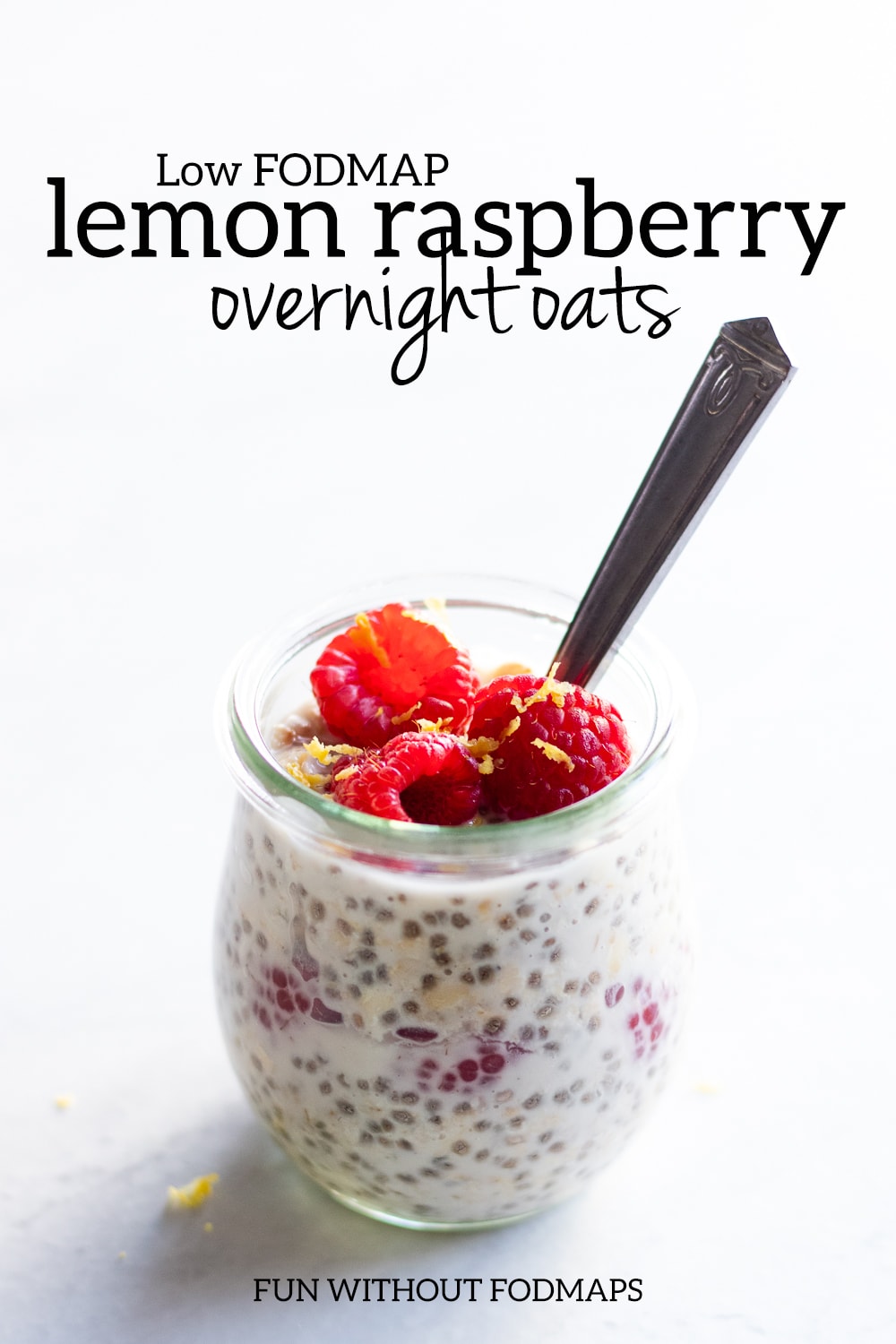 A tulip-shaped glass jar filled with overnight oats and fresh raspberries. Above, a black text overlay reads "Low FODMAP Lemon Raspberry Overnight Oats."