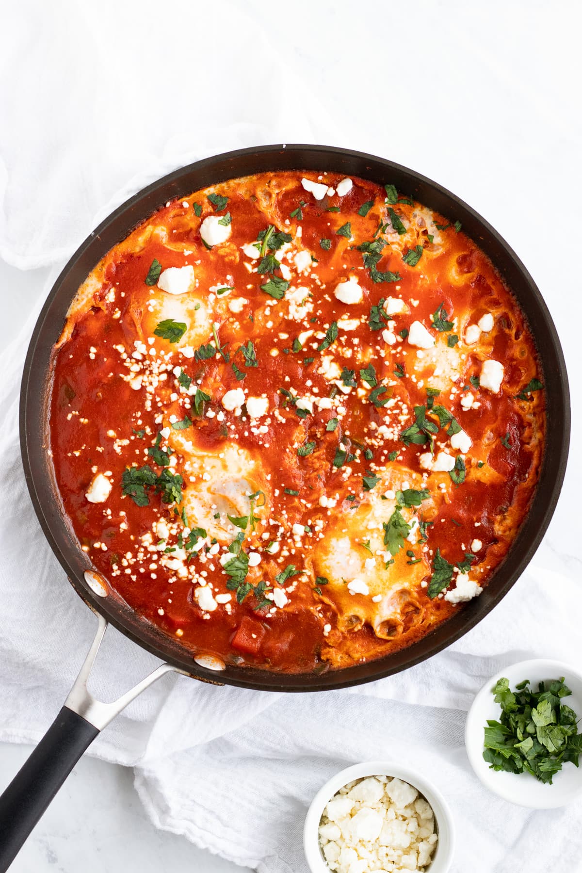 A skillet filled with yummy low FODMAP shakshuka. This spicy tomato dish with  poached eggs is topped with fresh parsley and creamy feta.