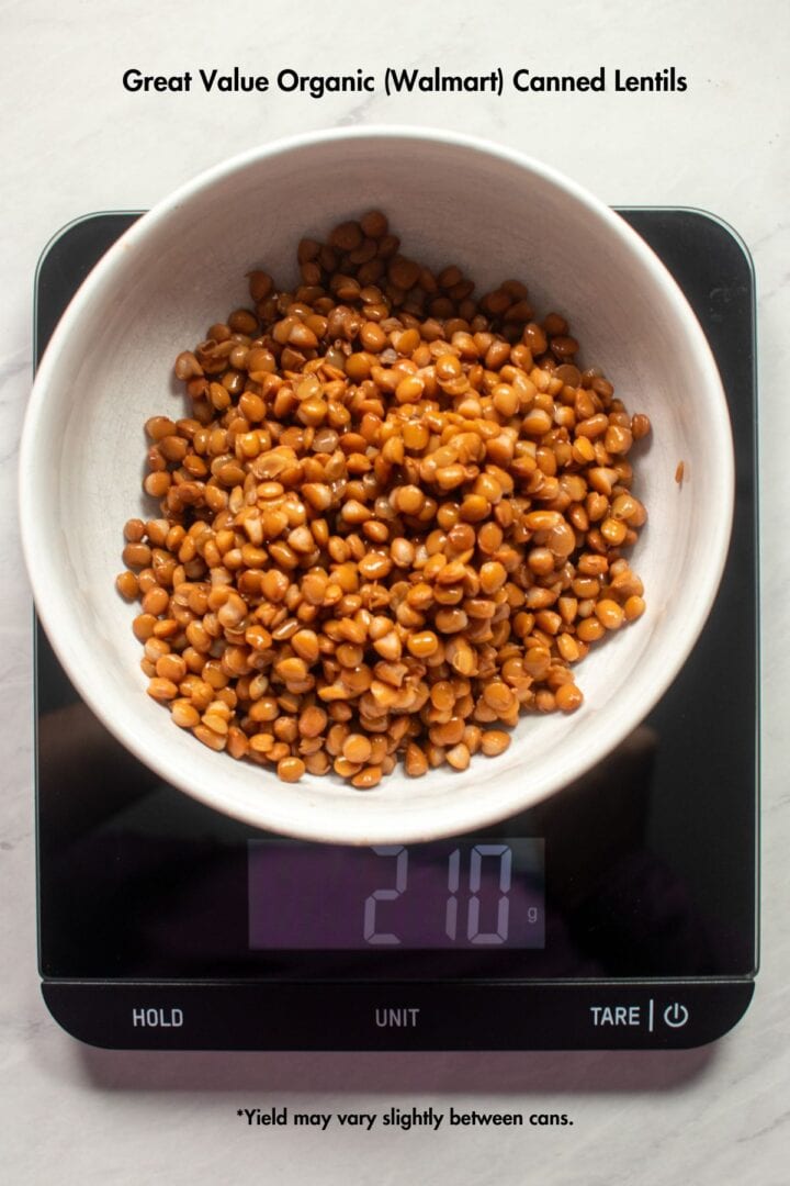 A rinsed and drained can of Walmart's Great Value Organic canned lentils in a bowl on a food scale. The food scale reads 210 gram. Black text in the white space above reads "Great Value Organic (Walmart) Canned Lentils." Text below the food scale reads "Yield may vary slightly between cans" 