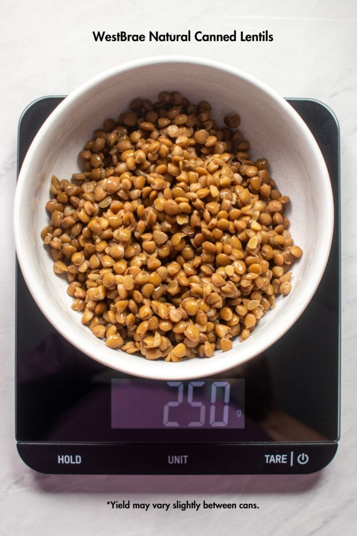 A rinsed and drained can of Westbrae Natural's canned lentils in a bowl on a food scale. The food scale reads 210 gram. Black text in the white space above reads "Westbrae Natural Canned Lentils." Text below the food scale reads "Yield may vary slightly between cans" 