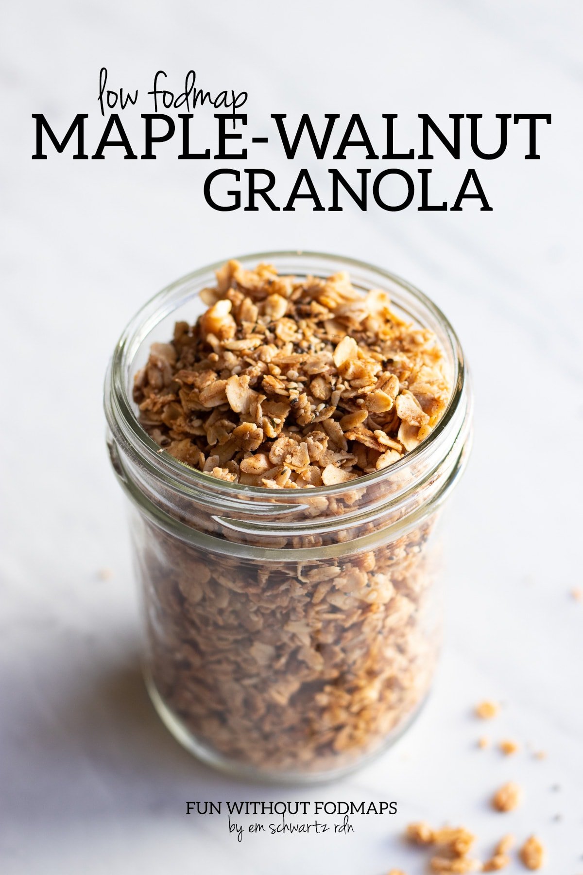 A mason jar filled with low FODMAP granola sitting on a white marble countertop. In the white space above, black text reads "Low FODMAP Maple-Walnut Granola."