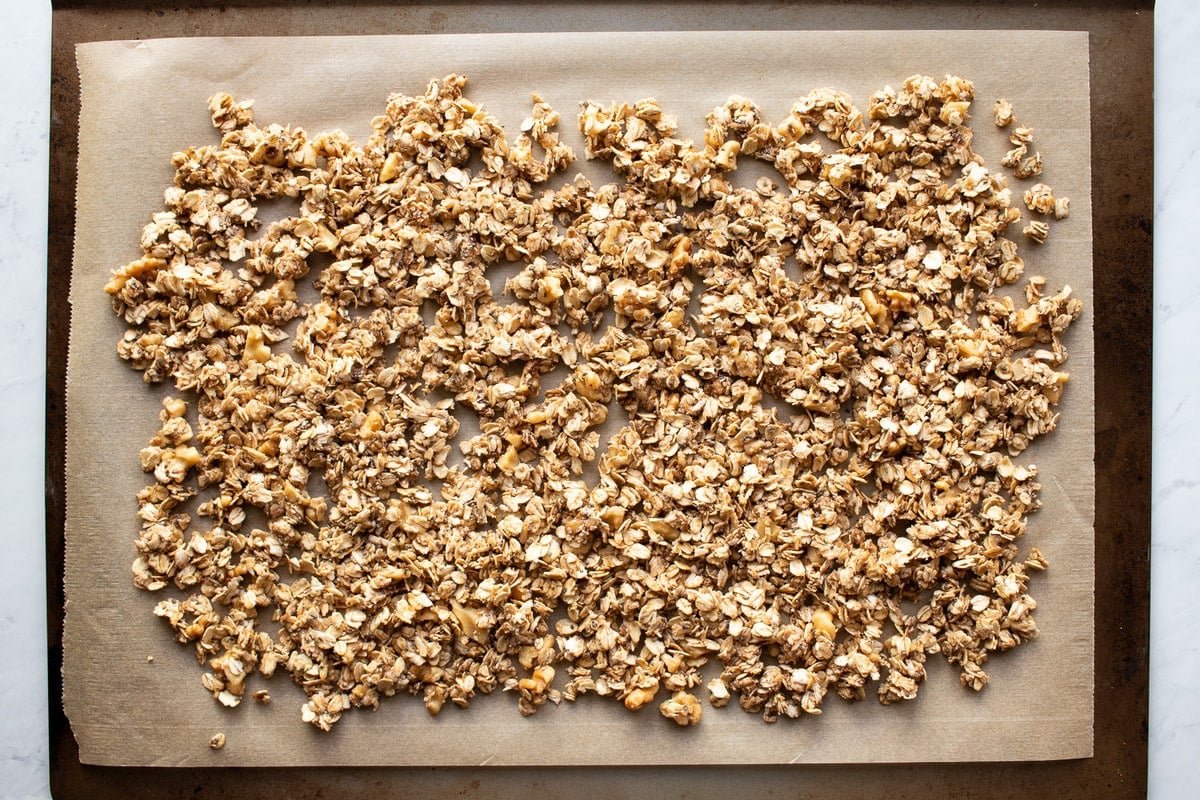 Granola mixture is spread in an even layer onto a baking sheet lined with brown parchment paper