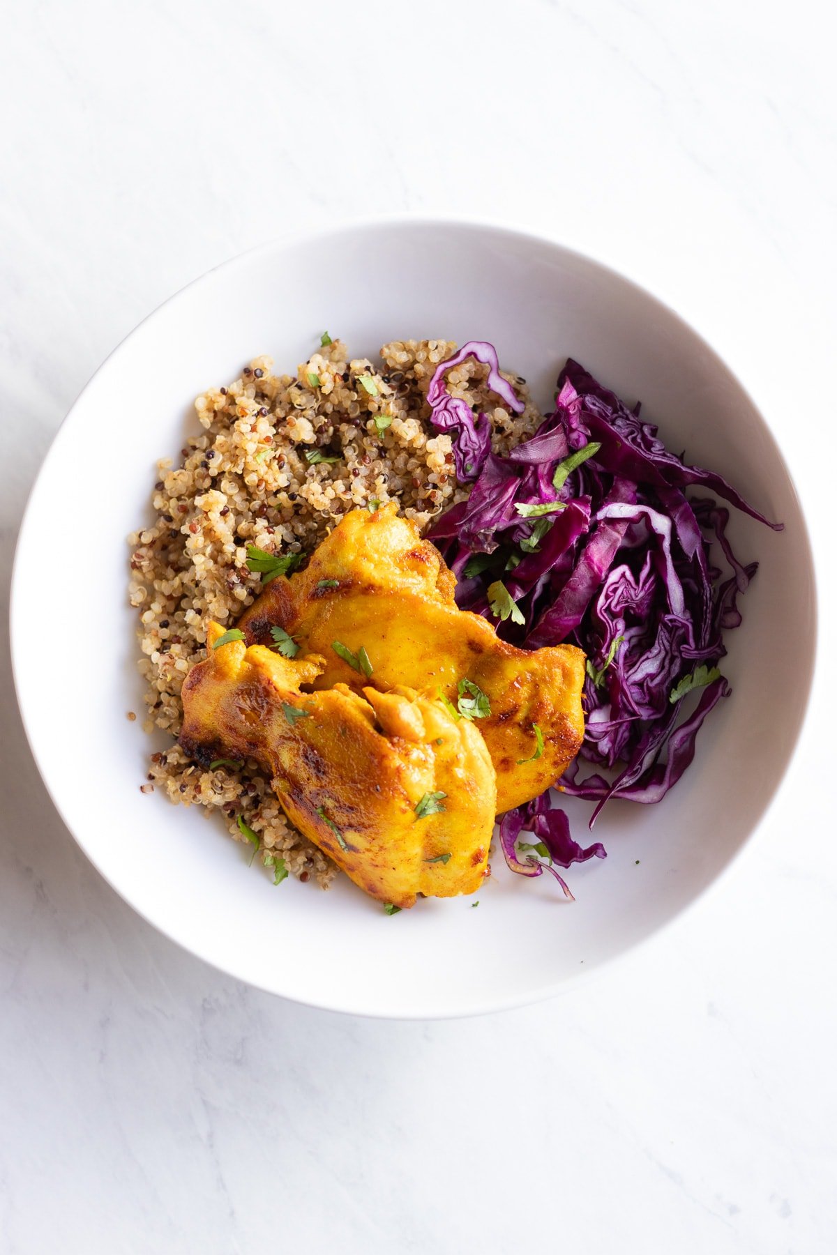 Looking down at a bowl of lemon-spiced chicken, red cabbage, and tri-color quinoa.
