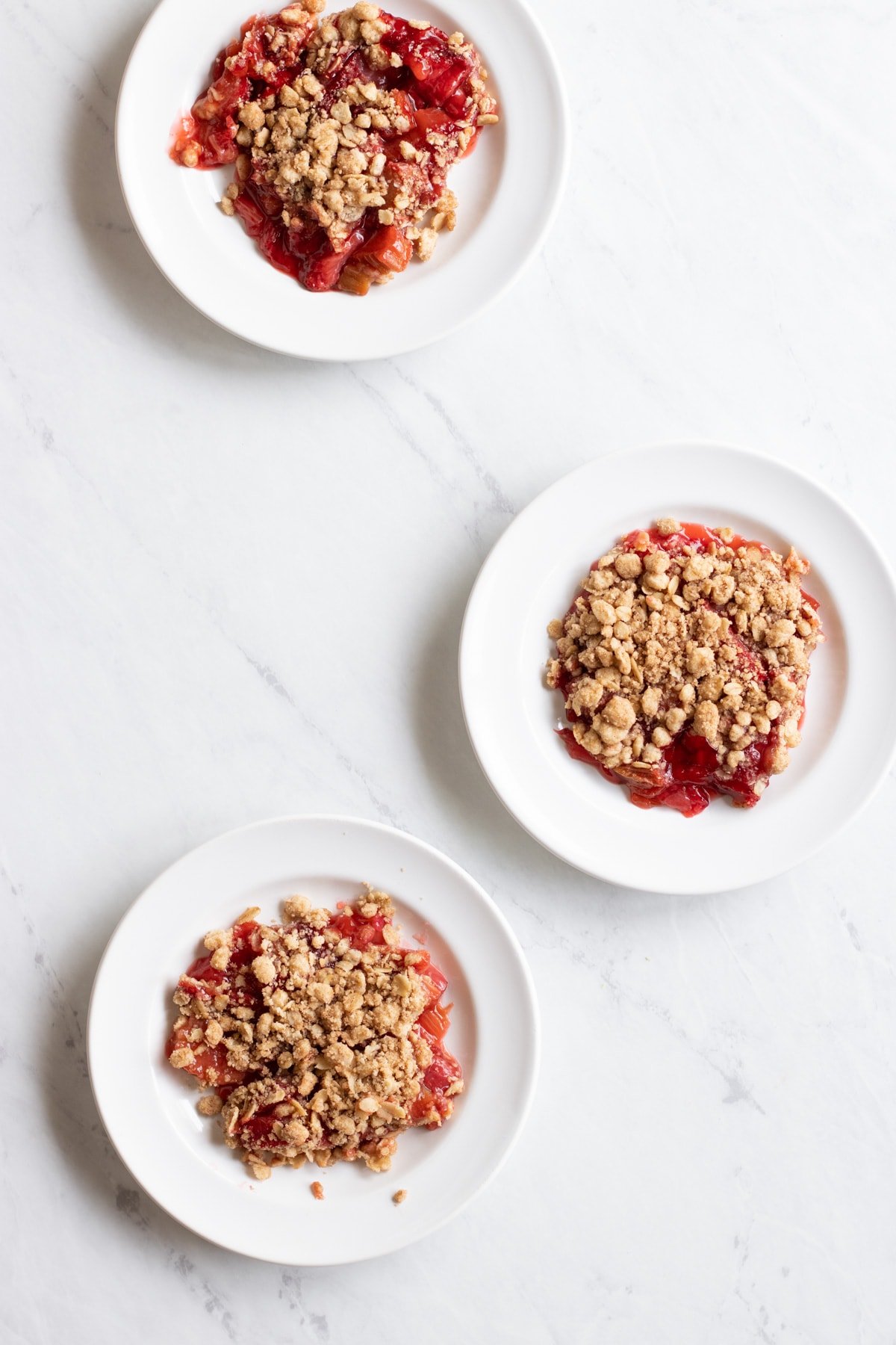 Three small white plates, each with a serving of low FODMAP strawberry rhubarb crumble.