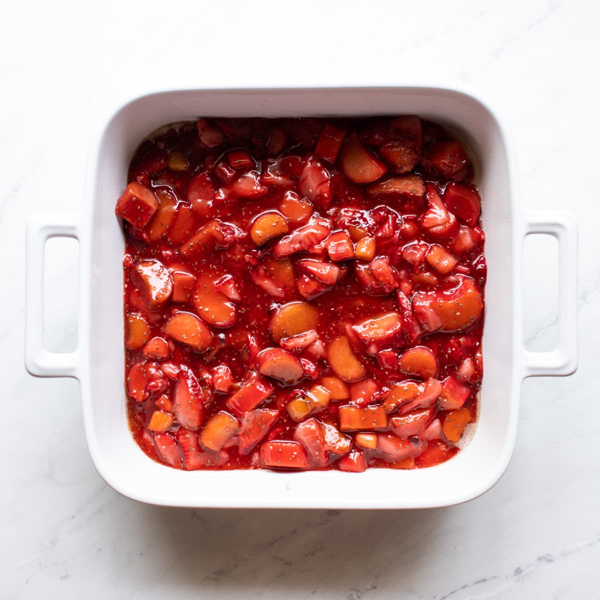 Syrupy strawberry rhubarb mixture has been transferred to a white baking dish coated with nonstick cooking spray.