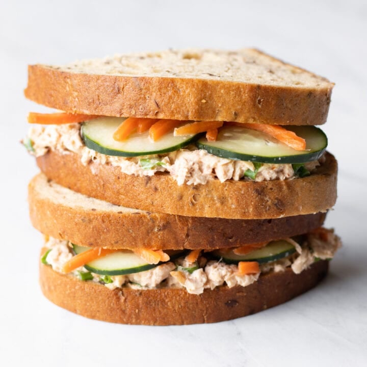 Halves of a low FODMAP spicy salmon salad sandwich are stacked on top of each other on a white marble slate.