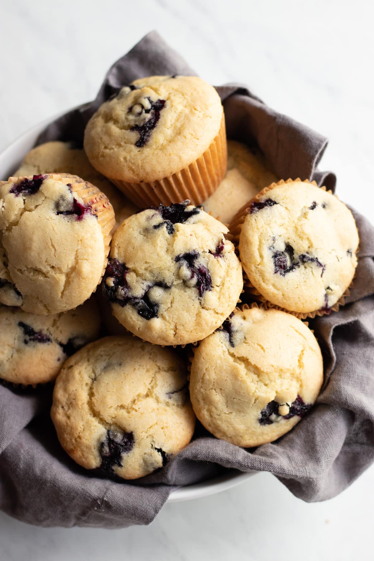 9 blueberry muffins in a bowl lined with a dark gray linen napkin