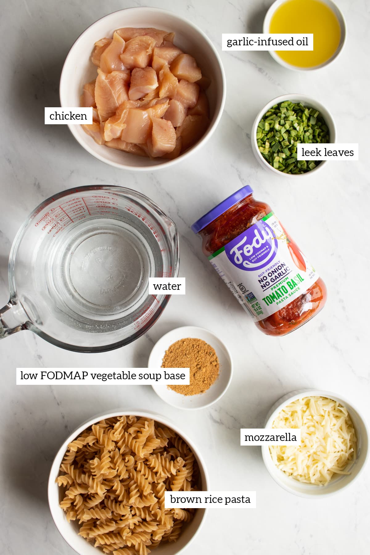 The ingredients needed to make this Instant Pot Low FODMAP Tomato-Basil Pasta are measured out into separate bowls on a marble countertop.