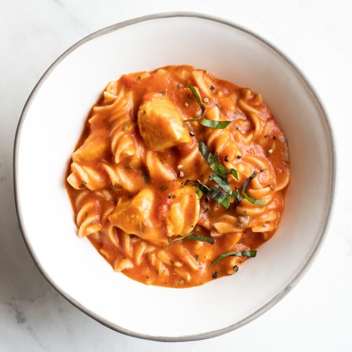 A bowl of creamy tomato basil fusilli pasta with chicken topped with finely shredded basil
