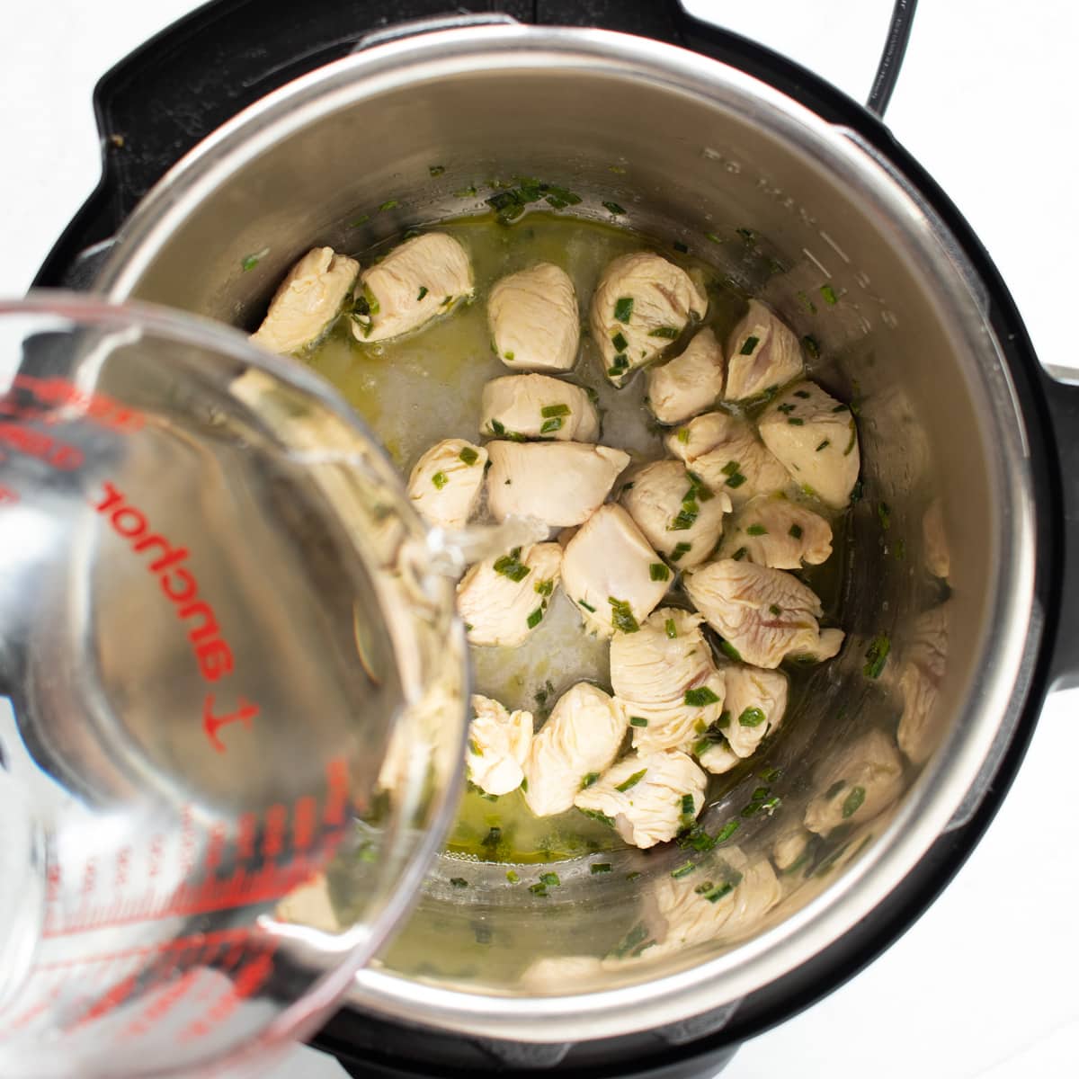Browned chicken and leek leaves in an Instant Pot with water being poured in to help deglaze the bottom of the pan.