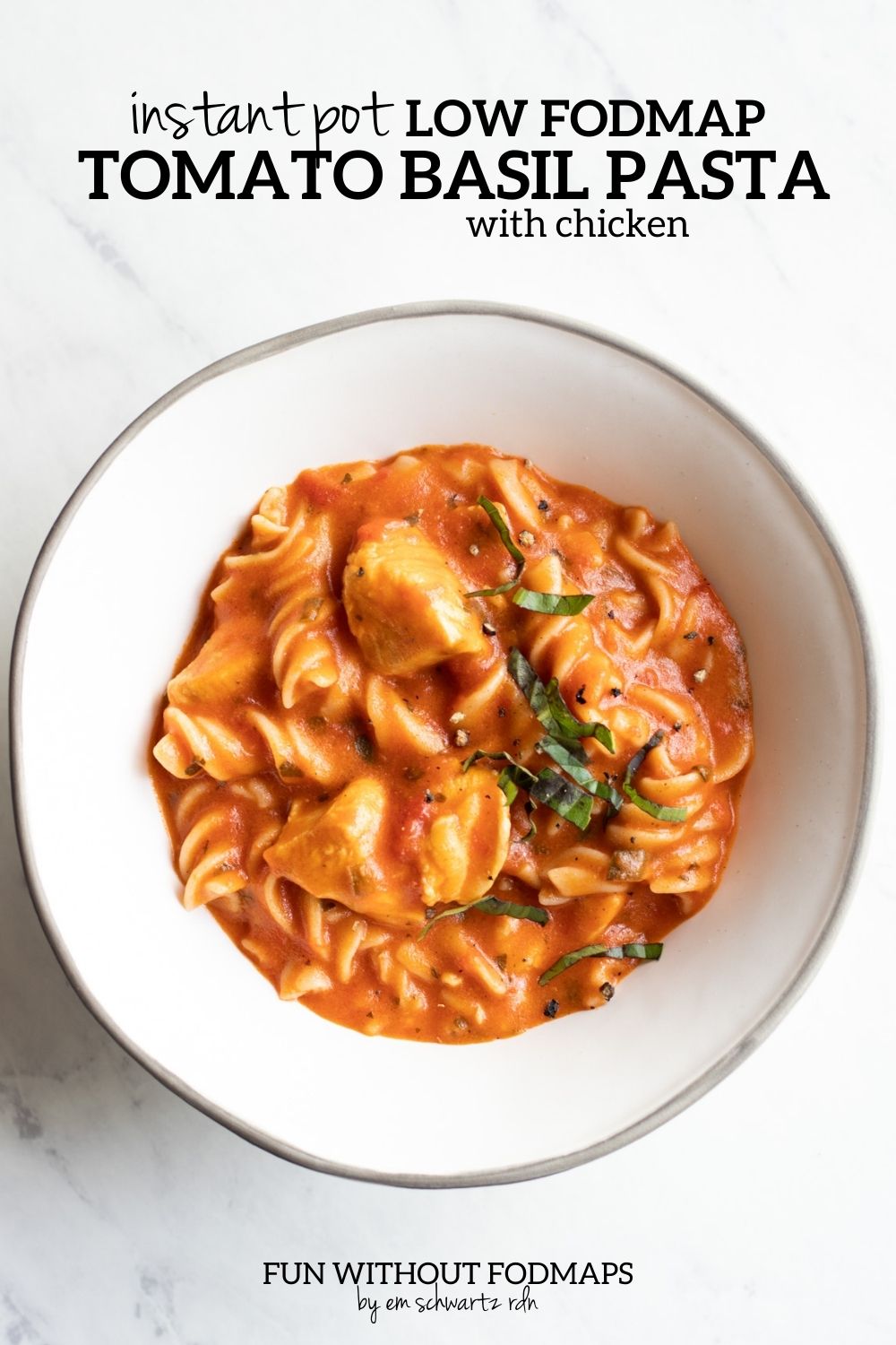 A white bowl filled creamy tomato-basil pasta. The bowl sits on a white marble countertop and above it a black text overlay reads Instant Pot Low FODMAP Tomato Basil Pasta with Chicken.