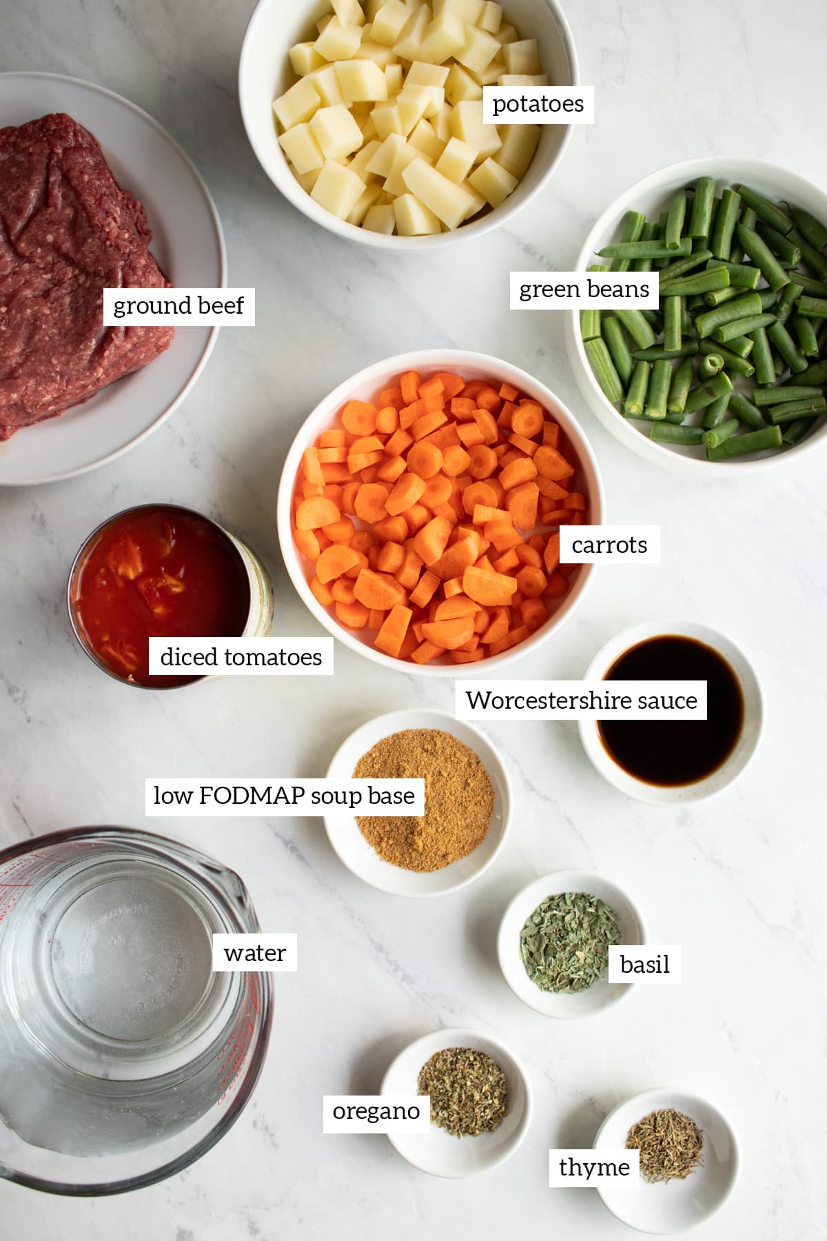 Ingredients needed to make Low FODMAP Hamburger Vegetable Soup are measured out into individual white bowls. 