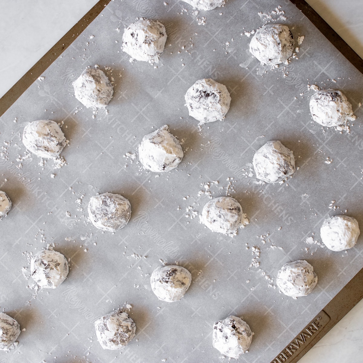 cookie dough balls rolled in powdered sugar on baking sheet